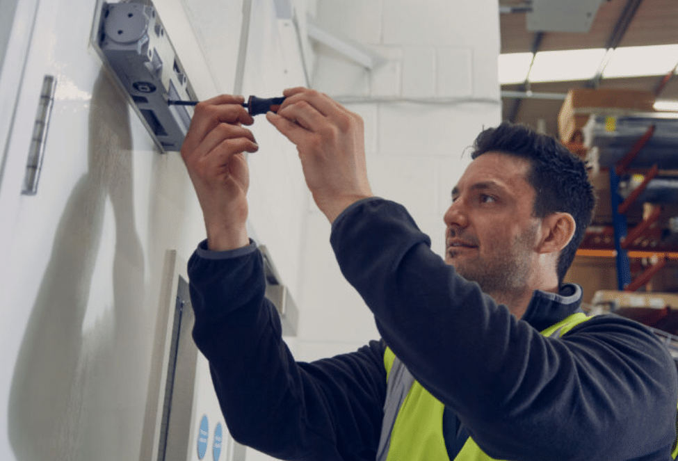 A man in hi vis vest maintaining a fire door